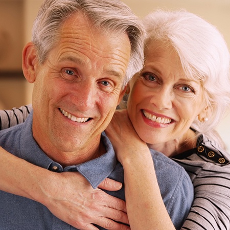 An older couple smiling and hugging in a home.