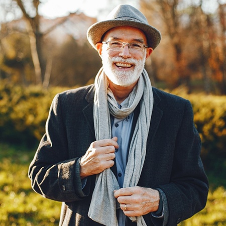 Older man with hat smiling with implant retained dentures
